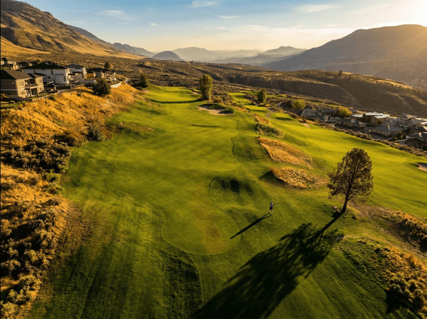 Aerial view of fairway and green at Bighorn Golf Kamloops with lone golfer and surrounding valley hills