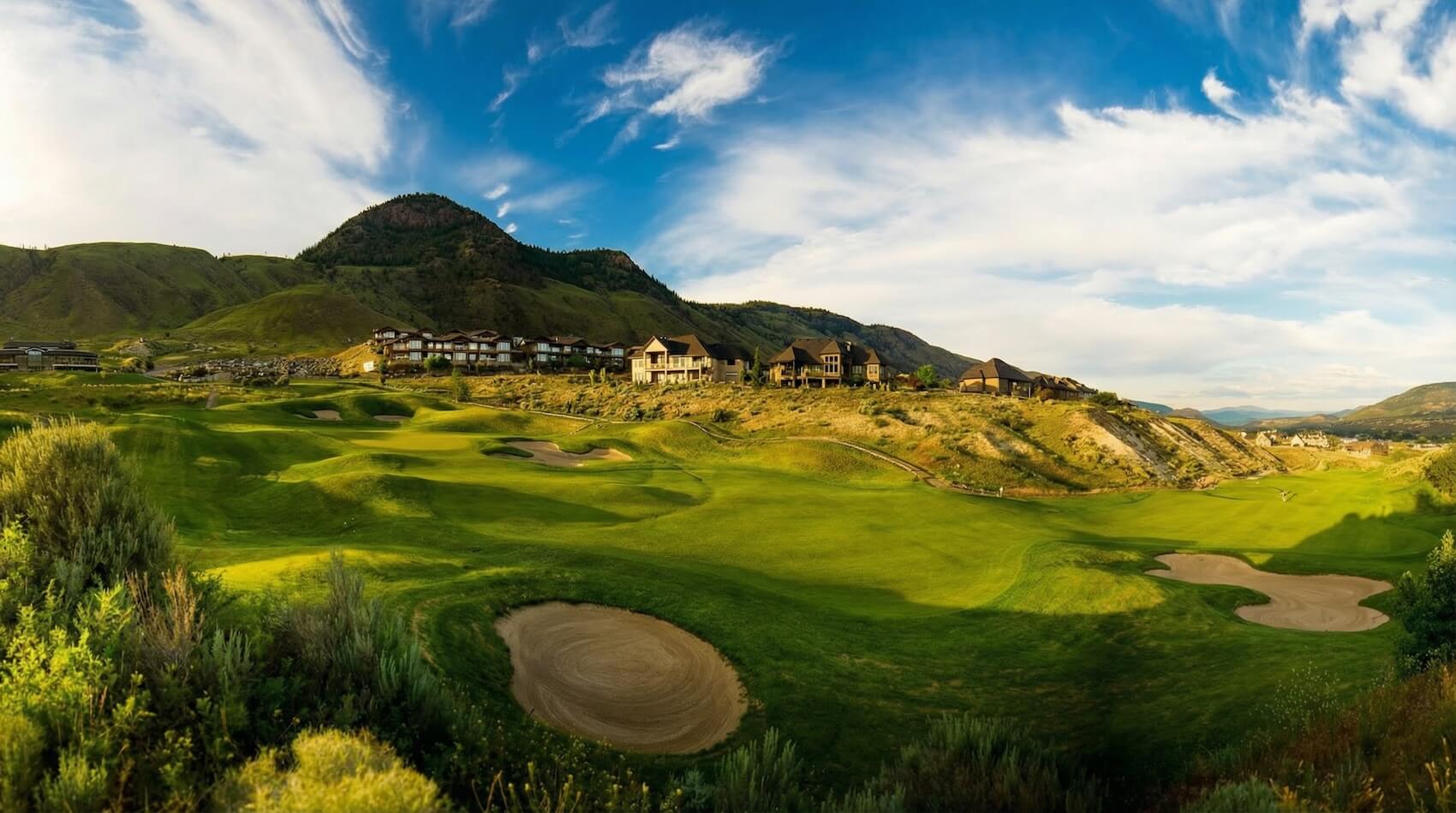 Wide view of rolling fairways and bunkers at Bighorn Golf Kamloops with hillside homes and mountain backdrop