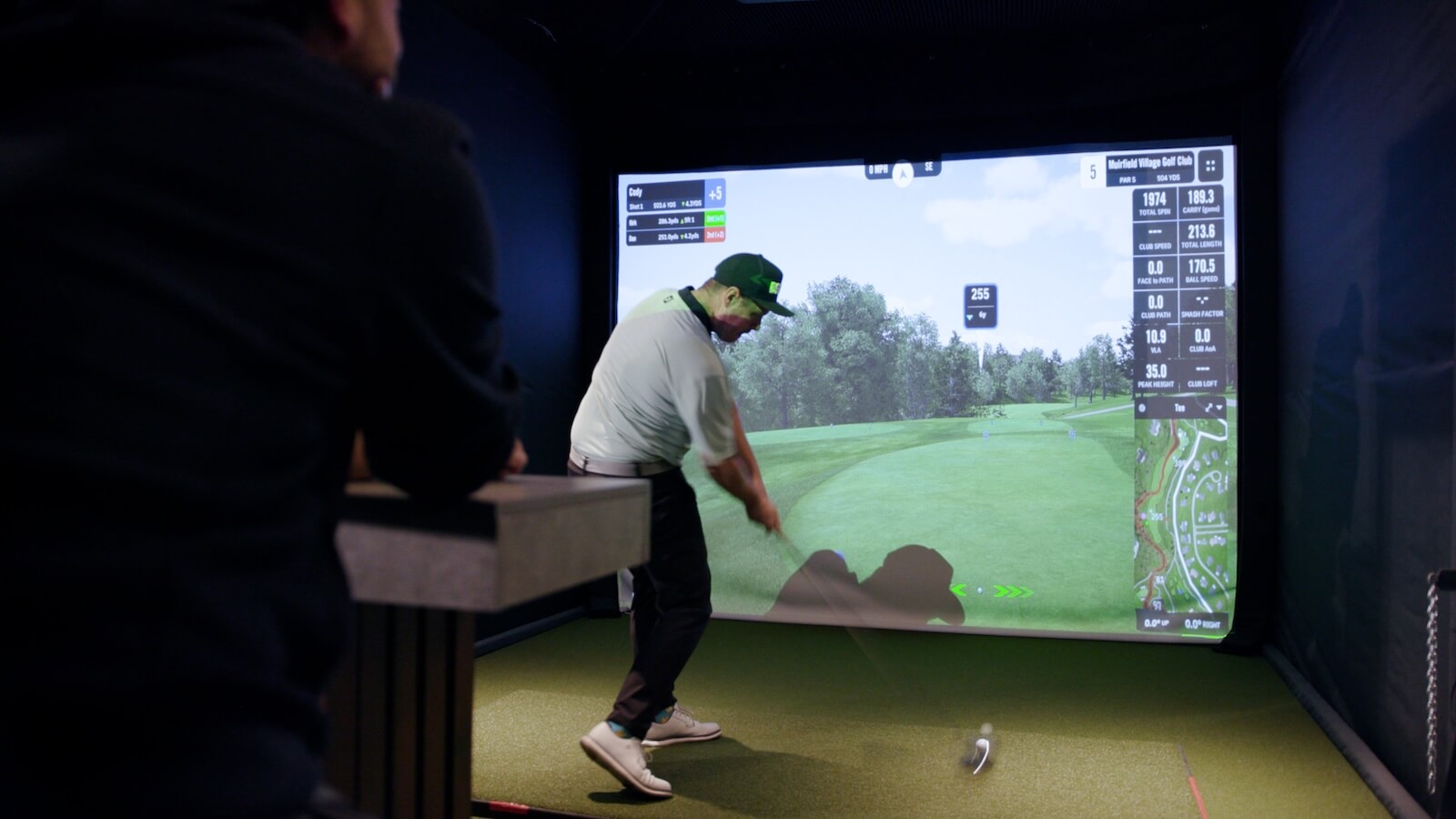 Golfer taking a swing on an indoor golf simulator with virtual course display and shot analytics
