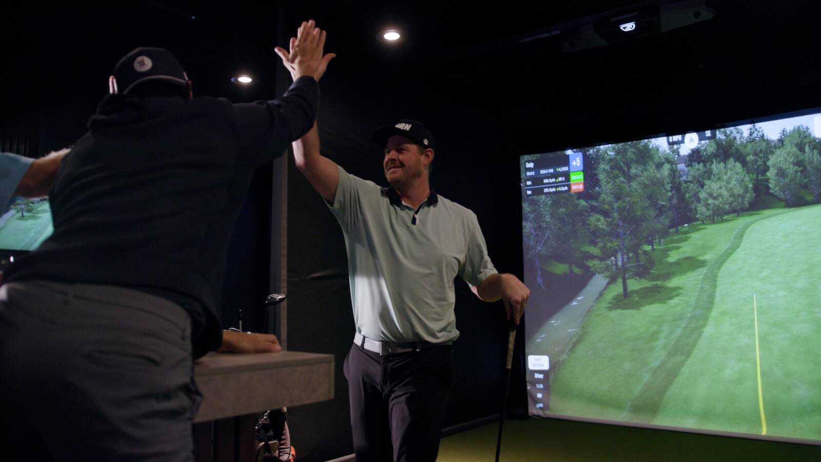 Golfers celebrating with a high five after a successful shot in indoor golf simulator lounge