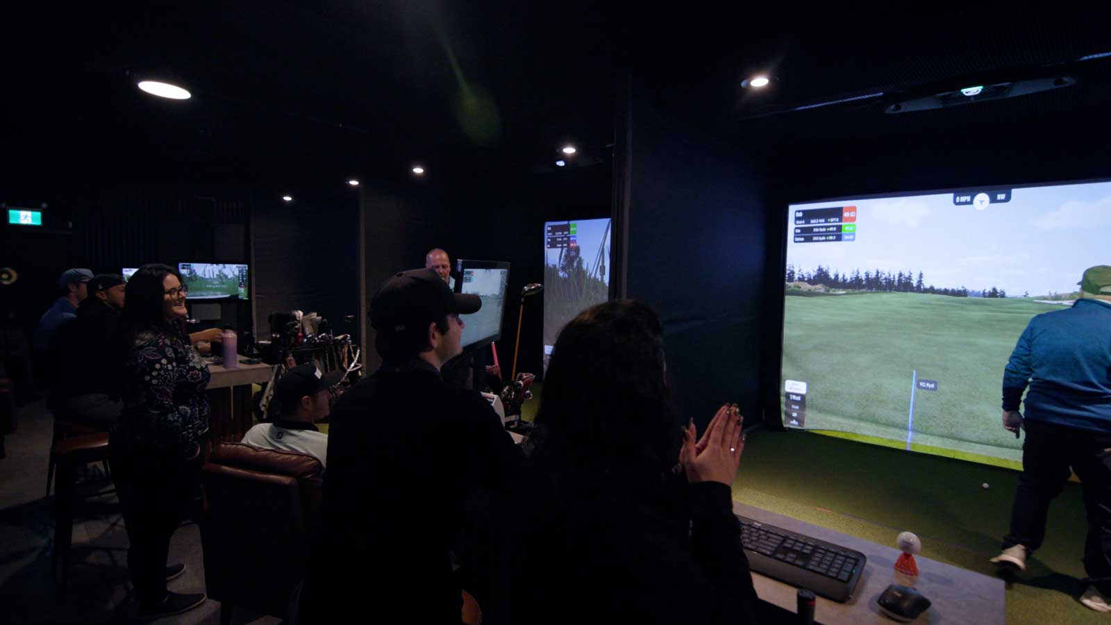 Group enjoying indoor golf simulator experience with virtual course display and social atmosphere