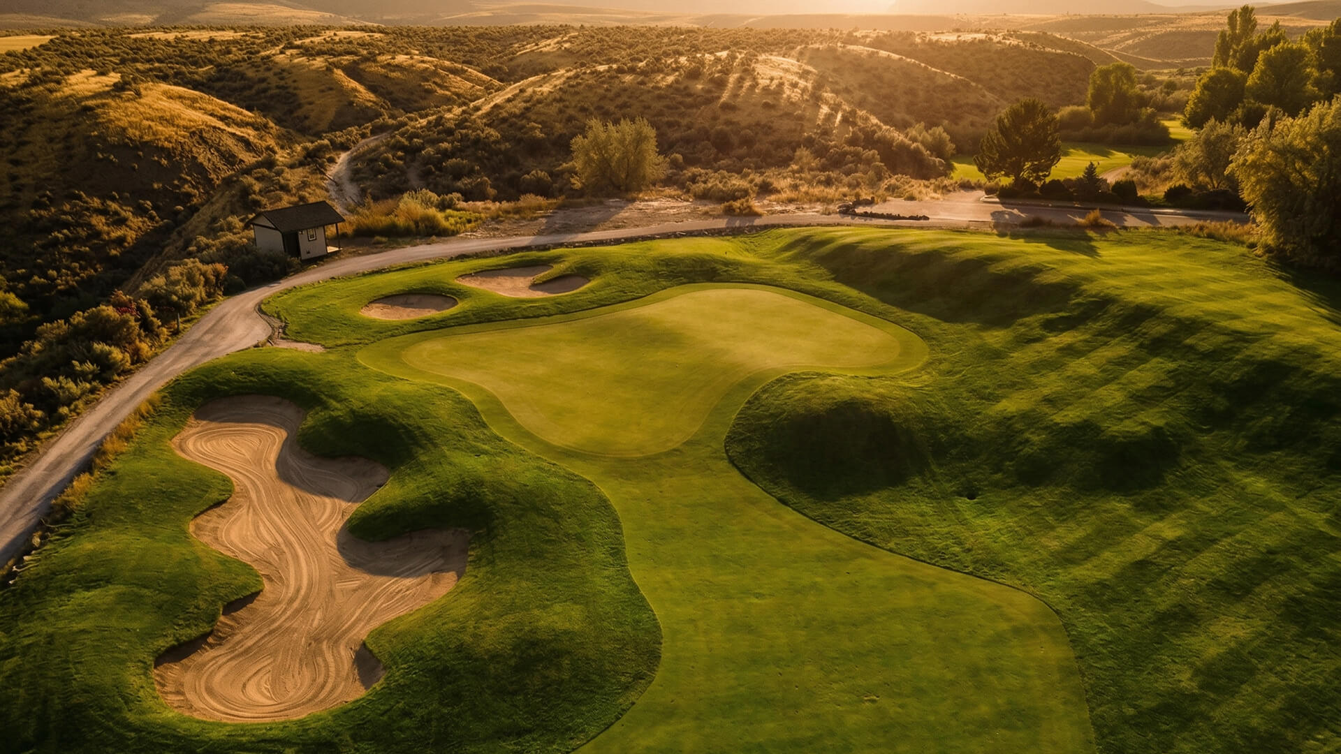 Elevated view of contoured green and bunkers at Bighorn Golf Kamloops with surrounding desert hills at sunset
