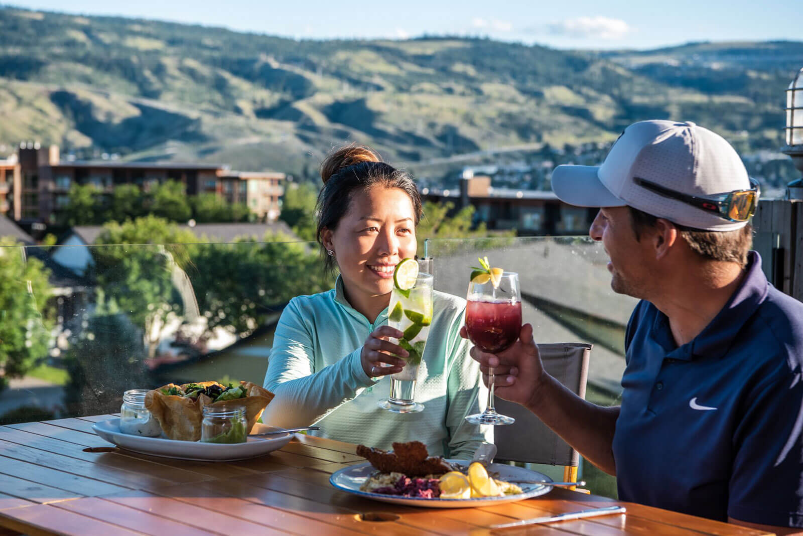 Couple enjoying drinks and patio dining with scenic mountain and golf course views at Bighorn Golf Kamloops